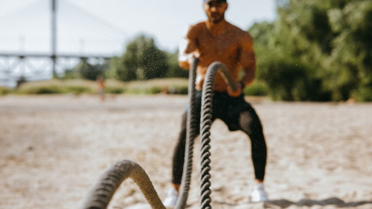Man exercising with battle ropes on a sunny beach, showcasing strength and determination.